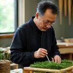 佐藤健太のポートレート。繊細な苔庭の模型を調整している。